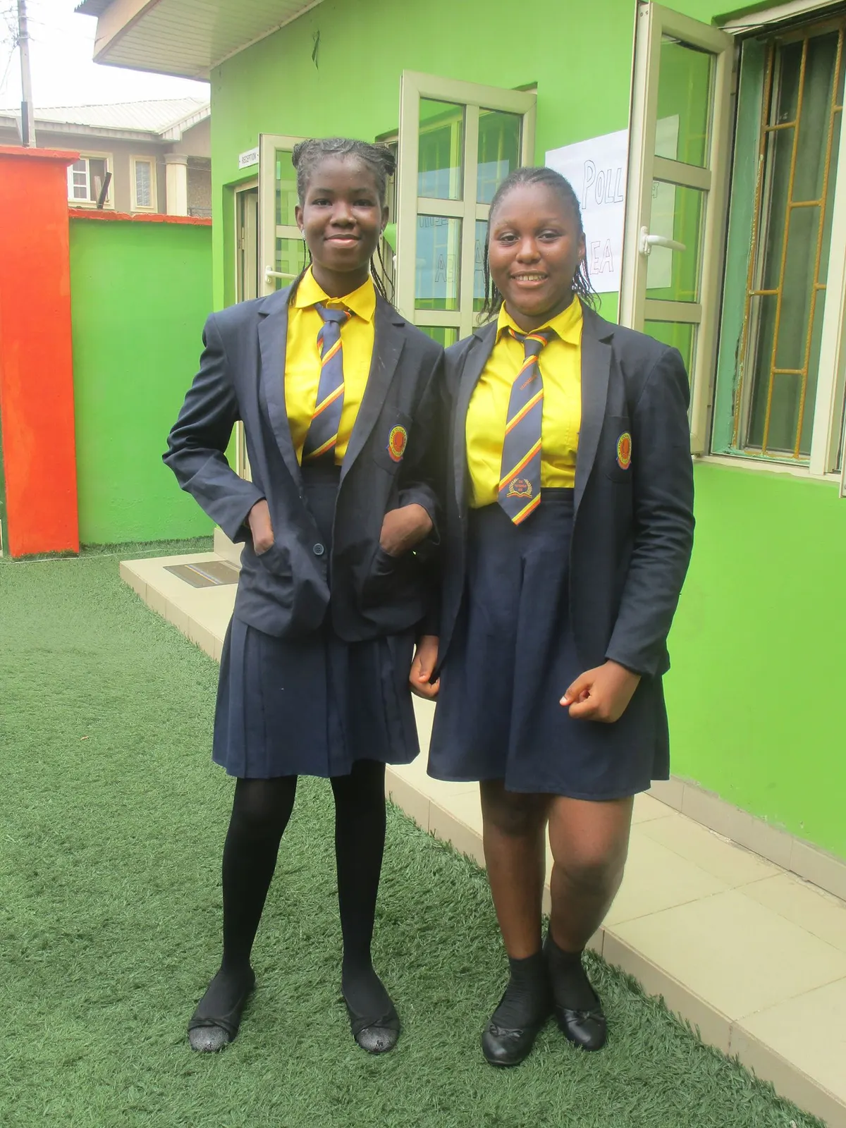 Two students in navy blazers smiling in the school grounds