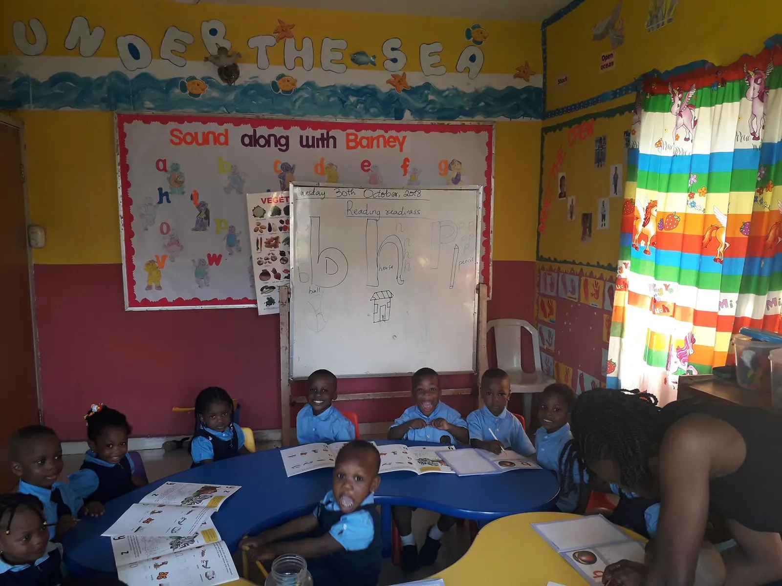 Young children seated around a table in a brightly decorated classroom