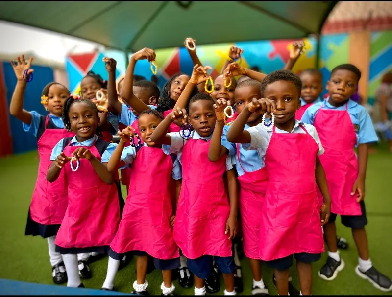 Smiling Olivesfield pupils in aprons holding up bead bracelets they have made