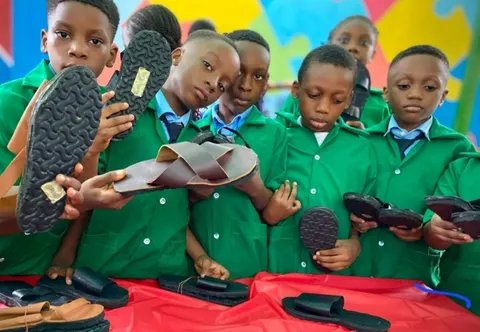 Pupils in green uniforms showing sandals they have made in a practical skills session