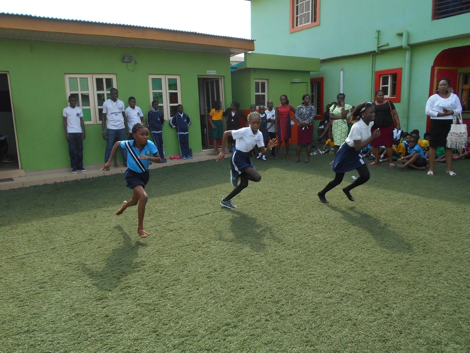 Pupils running a race on the school field while classmates watch