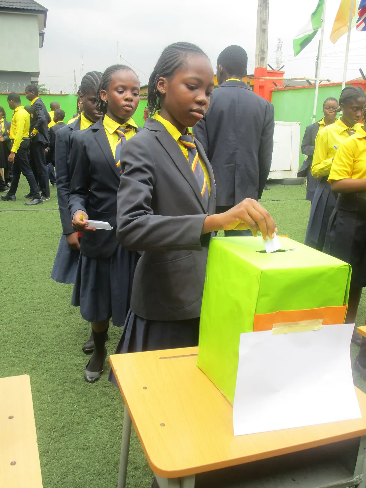 Students in school uniform queueing to cast their votes in a ballot box on the school field