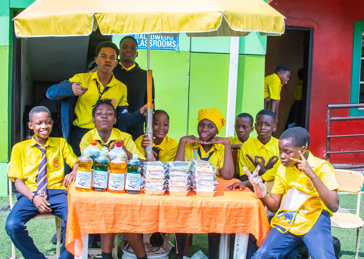Students seated at a stall displaying drinks and snacks they prepared for sale